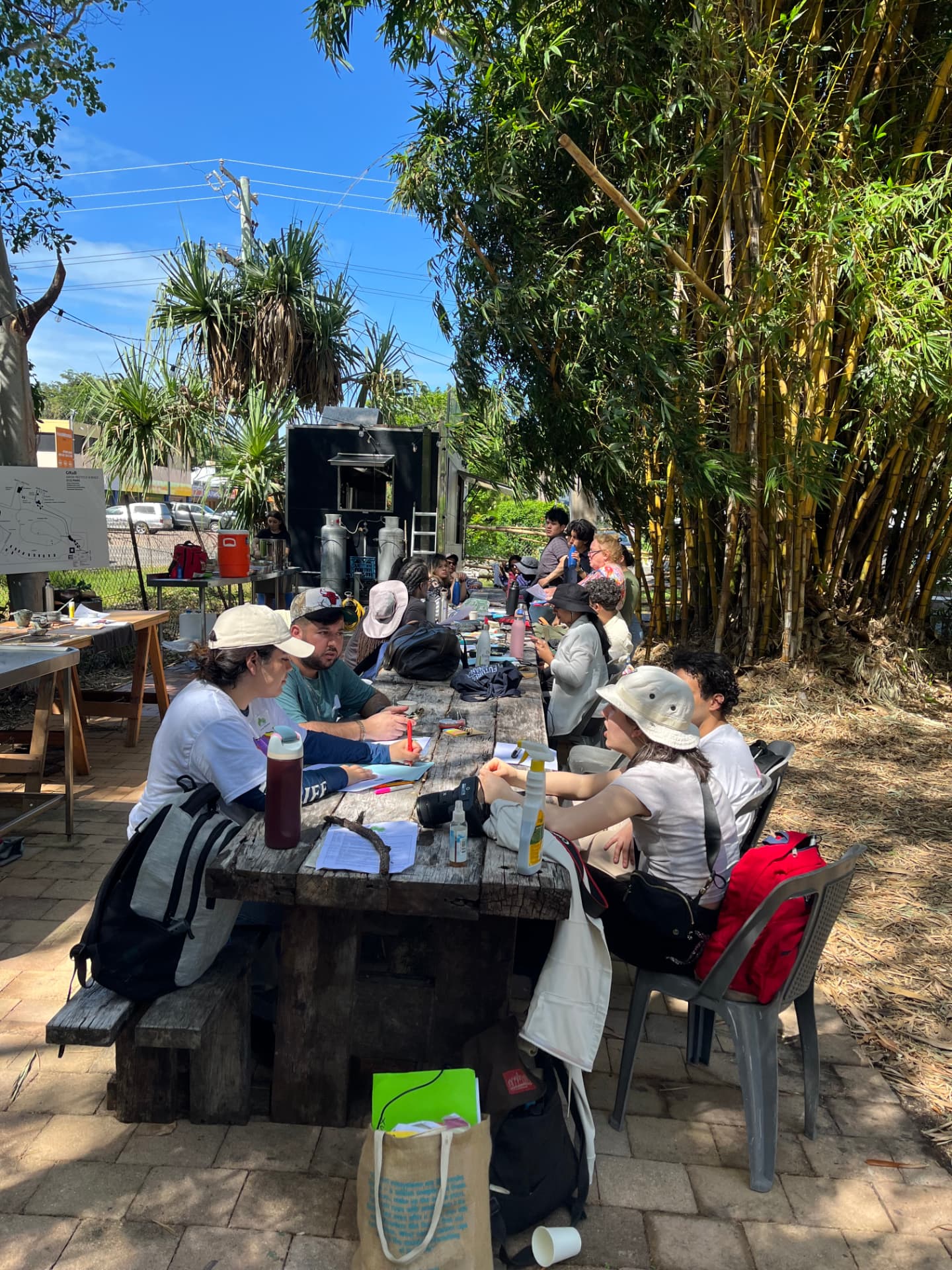 CUNY students working together at the long table beneath the bamboo